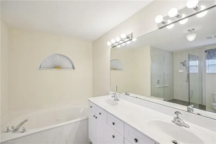 Bathroom featuring a tub with jets, a stall shower, and double vanity