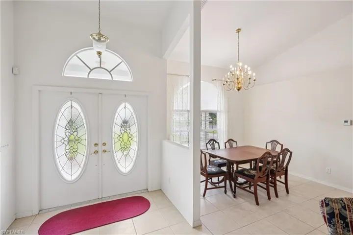 Dinning and foyer entrance with a chandelier, healthy amount of natural light, vaulted ceiling, and light tile patterned flooring