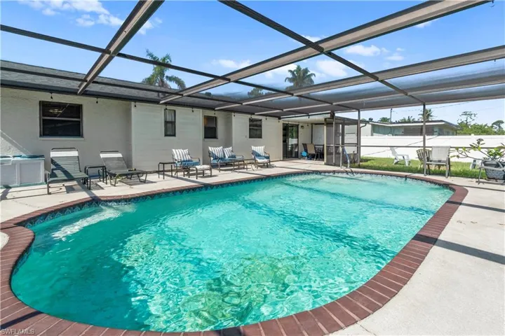 Screened outdoor swimming pool area with a concrete pool deck and brick coping