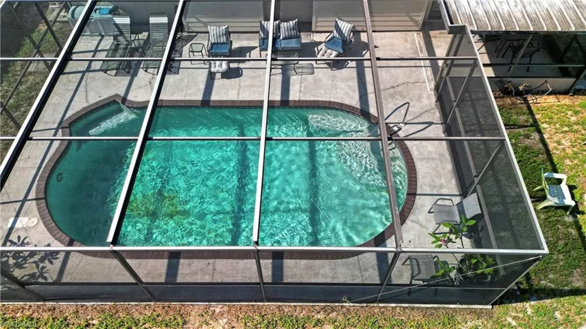 Screened-in pool area featuring a kidney-shaped swimming pool with a concrete surround and a paver coping
