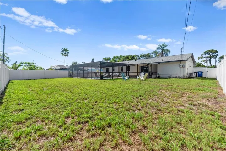 Large backyard featuring a privacy fence, screened-in pool enclosure, and covered patio space