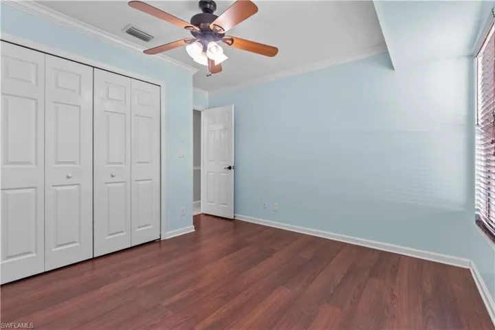 Spacious room featuring wood-finish flooring, light blue walls, and white crown molding