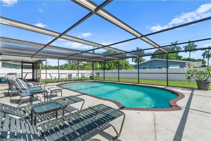 Screened-in pool area featuring a freeform swimming pool, concrete deck, and brick coping