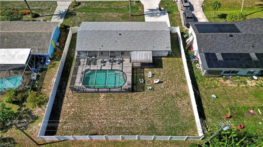 Fenced property featuring an oval-shaped screened pool, an expansive lawn, and an attached covered patio