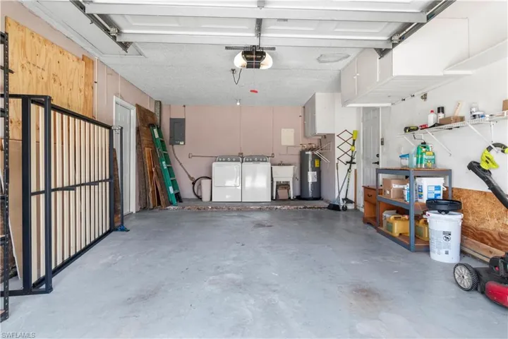 Attached single-car garage featuring a concrete floor, overhead garage door, built-in overhead storage cabinets, and laundry hookups with a utility sink
