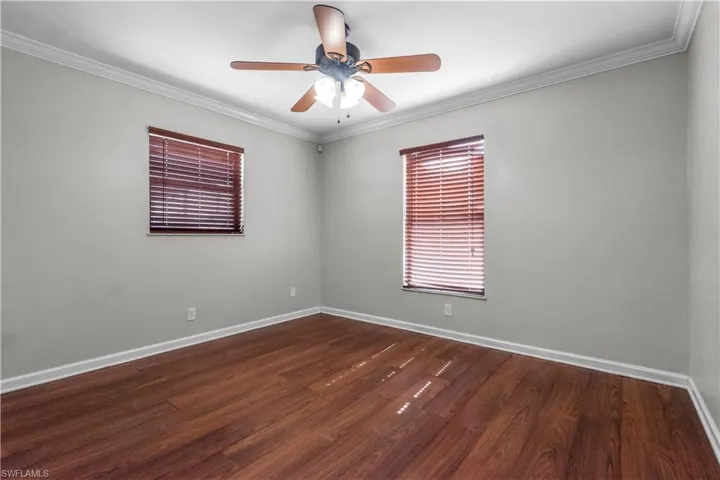 Primary Ensuite featuring wood-finish flooring, two windows with horizontal blinds, a ceiling fan with integrated lighting, and crown molding