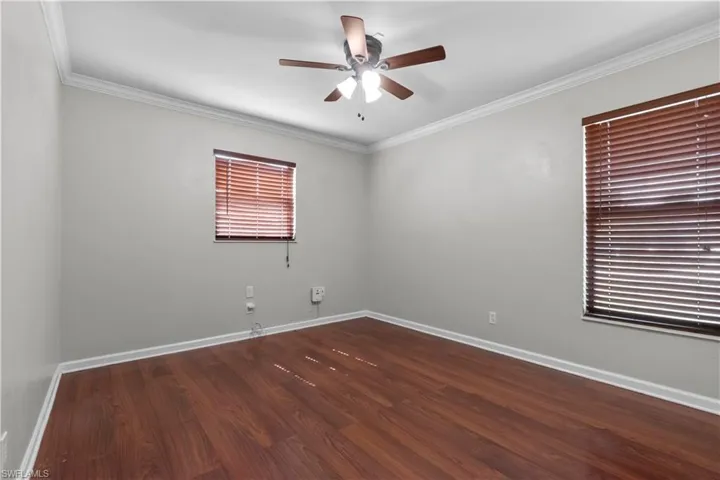 Third bedroom featuring wood-finish flooring, two windows with horizontal blinds, and a ceiling fan with integrated lighting
