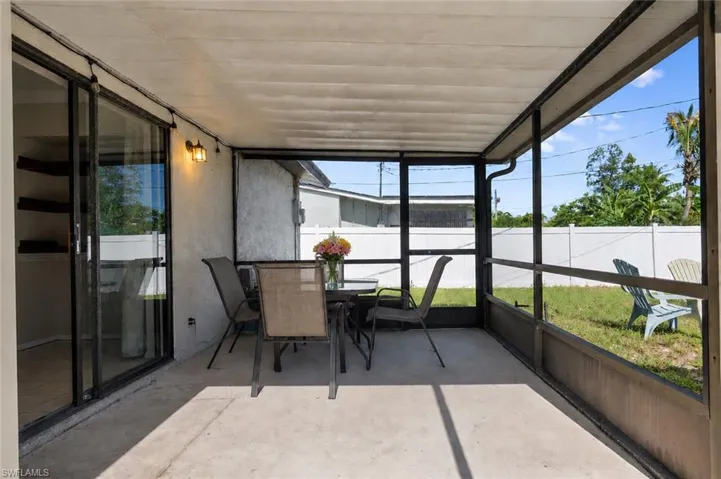 Screened concrete patio featuring an exterior wall sconce, sliding glass door access, and a perimeter privacy fence