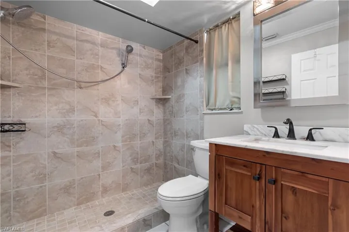 Walk-in shower with natural stone-look tile, integrated shelving, and a handheld showerhead