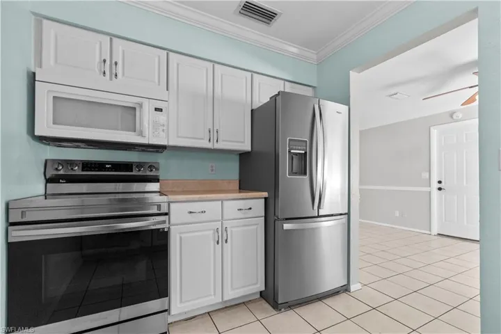 Kitchen featuring white cabinetry, stainless steel appliances, light-toned countertops, and tile flooring