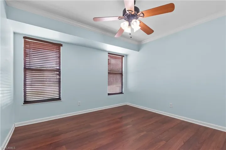 Second bedroom featuring wood-finish flooring, two windows with blinds, a ceiling fan with integrated lighting, and crown molding