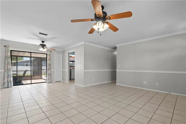 Great room featuring neutral tone ceramic tile flooring, a large sliding glass door leading to the pool, crown molding, and a chair rail accent.