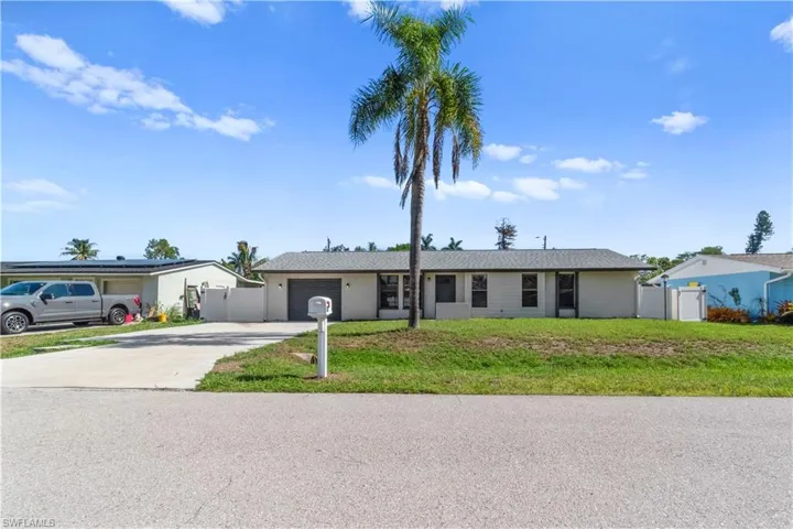 Single-story residence featuring a gray asphalt shingle roof, a two-car concrete driveway, a prominent palm tree, and a white fence enclosing a portion of the property