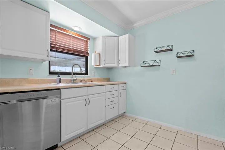 Kitchen featuring white cabinetry, light-toned countertops, a stainless steel dishwasher, and a window with blinds