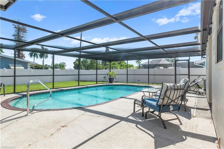 Screened-in outdoor pool area featuring a rectangular pool with a curved edge, concrete pool deck, and white privacy fencing