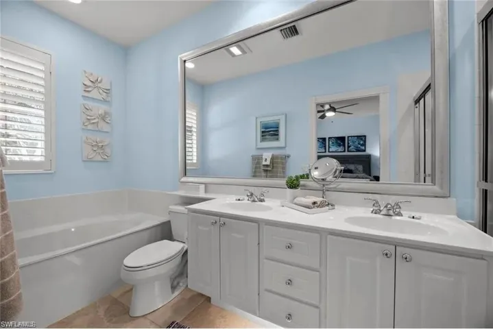 Bathroom featuring a large vanity with dual sinks, white cabinetry, and a spacious bathtub