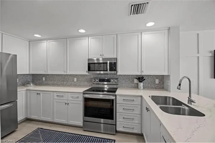The kitchen features white cabinetry, stainless steel appliances, and a double basin sink