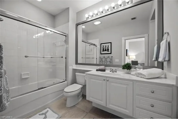 Bathroom featuring a white vanity with a white countertop and a large framed mirror with overhead lighting