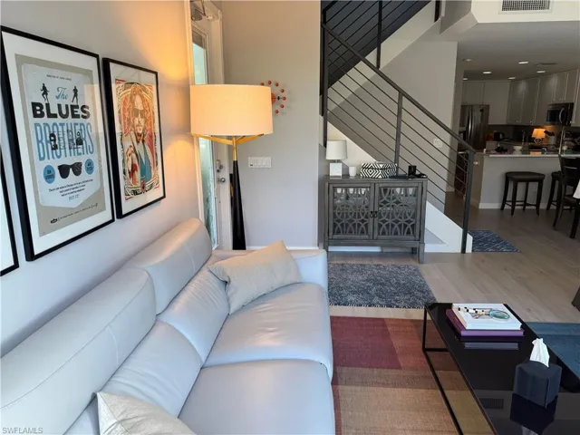 The living area features light wood flooring, a contemporary staircase with metal railings, and an open layout that extends to the kitchen