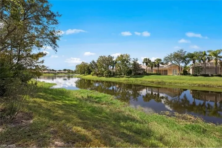 Lush, green landscaping and mature trees frame the tranquil water feature, with properties visible in the background
