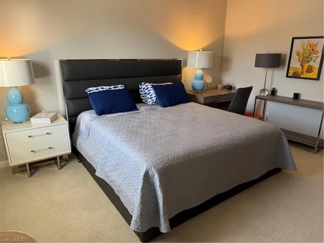 This room features a neutral color palette, carpet flooring, and a bed with a dark upholstered headboard