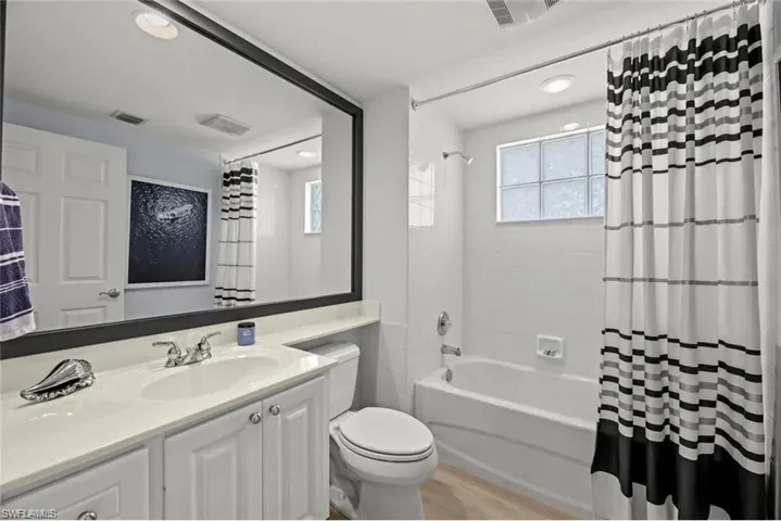 The bathroom features a vanity with a white countertop and cabinet storage, a large mirror, a toilet, and a bathtub with a shower and white tile surround