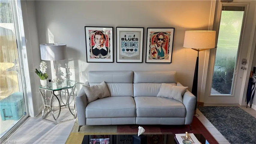 The living area features light-colored walls, a large window, and a glass-paneled door