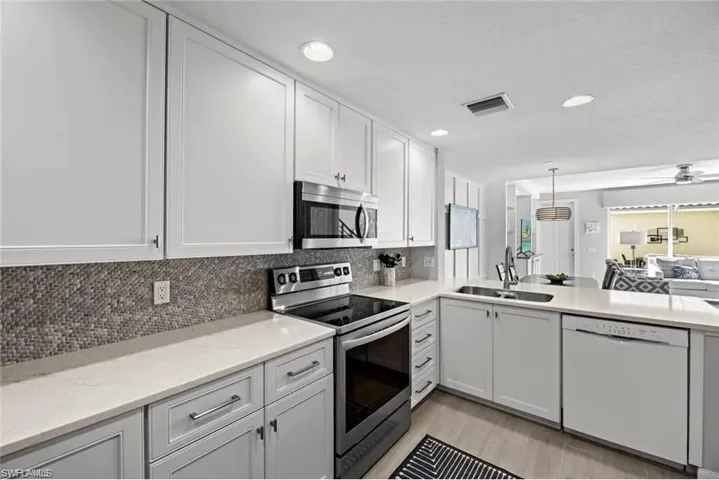 The kitchen features white upper cabinetry, light gray lower cabinetry, and a mosaic tile backsplash