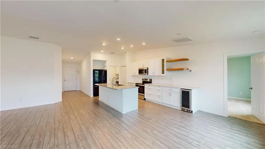 Kitchen featuring beverage cooler, white cabinets, stainless steel appliances, and sink
