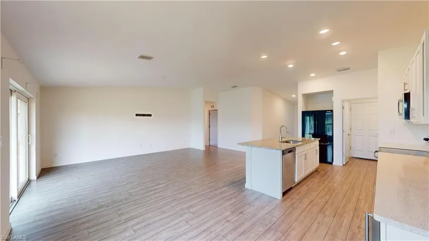 Kitchen featuring white cabinets, light hardwood / wood-style flooring, light stone counters, stainless steel appliances, and a center island with sink