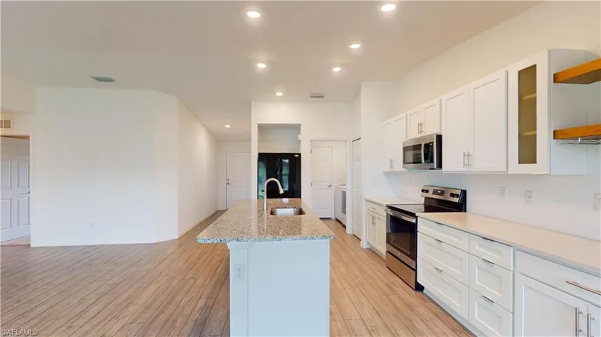 Kitchen featuring appliances with stainless steel finishes, white cabinetry, an island with sink, and light hardwood / wood-style floors