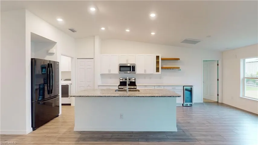 Kitchen featuring white cabinetry, vaulted ceiling, an island with sink, light stone countertops, and appliances with stainless steel finishes