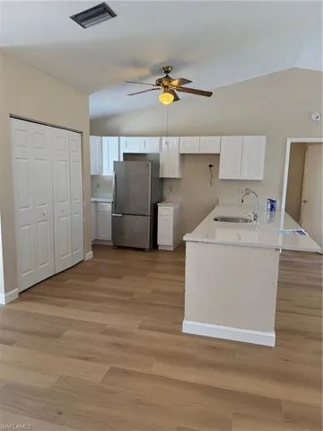 Kitchen featuring lofted ceiling, white cabinetry, freestanding refrigerator, a peninsula, and light stone countertops