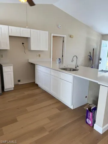 Kitchen featuring white cabinets, lofted ceiling, light wood-type flooring, light stone countertops, and a peninsula