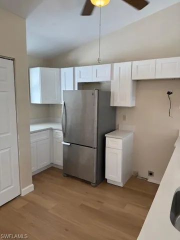 Kitchen featuring white cabinetry, freestanding refrigerator, lofted ceiling, ceiling fan, and light wood-style flooring