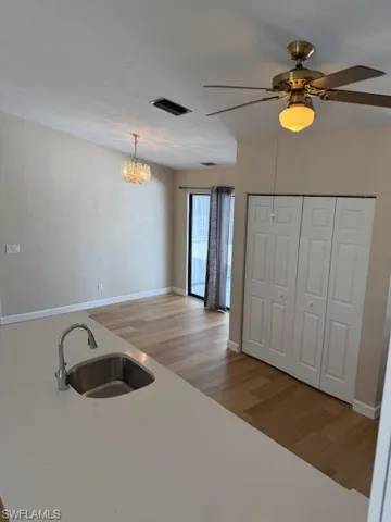 Kitchen featuring light wood-style floors, a ceiling fan, hanging light fixtures, a chandelier, and light stone counters