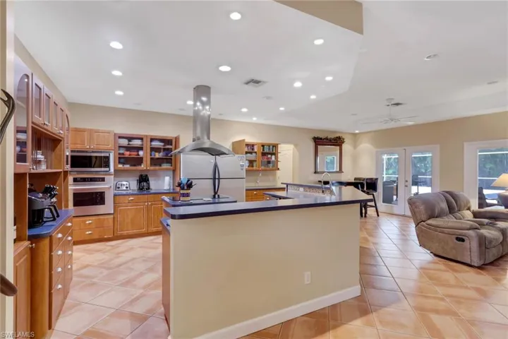 Spacious kitchen featuring warm wood cabinetry, stainless steel appliances, a central island with a breakfast bar, recessed lighting, and tile flooring