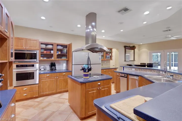 Spacious kitchen featuring wood cabinetry, blue countertops, stainless steel appliances, and an island with a built-in cooktop