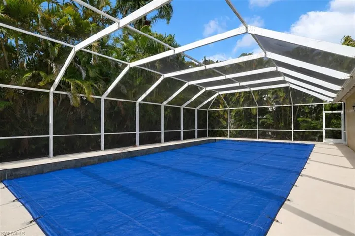 Screen-enclosed pool area featuring a blue pool cover, surrounding concrete deck, and a white aluminum frame