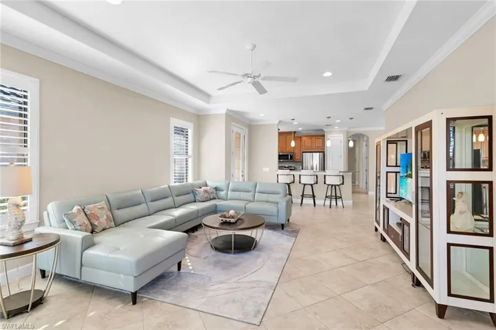 Living area with crown molding, ceiling fan, recessed lighting, a raised ceiling, and arched walkways