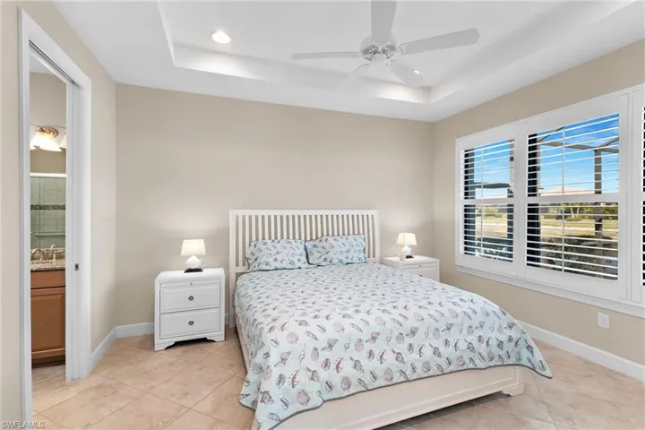 Bedroom with a raised ceiling, recessed lighting, ceiling fan, light tile patterned floors, and ensuite bath