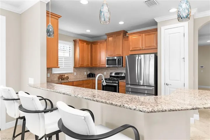 Kitchen with stainless steel appliances, ornamental molding, arched walkways, decorative backsplash, and light stone countertops
