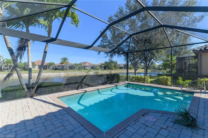Outdoor pool featuring glass enclosure, a water view, a patio area, and a sunroom