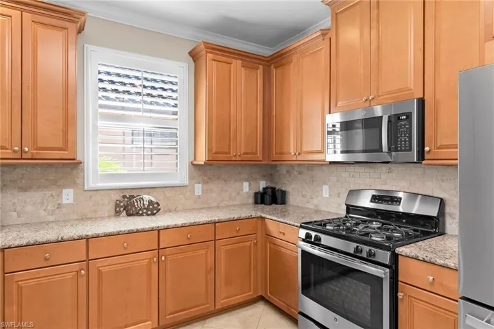 Kitchen featuring stainless steel appliances, light stone countertops, wood finish cabinets, decorative backsplash, and crown molding