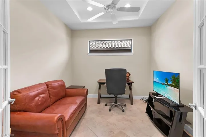 Home office with ceiling fan, a tray ceiling, and light tile patterned flooring