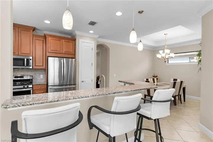 Kitchen with a kitchen breakfast bar, arched walkways, stainless steel appliances, light stone counters, and wood finish cabinets