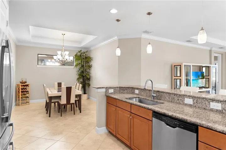 Kitchen with crown molding, stainless steel appliances, a tray ceiling, light stone countertops, and wood finish cabinets