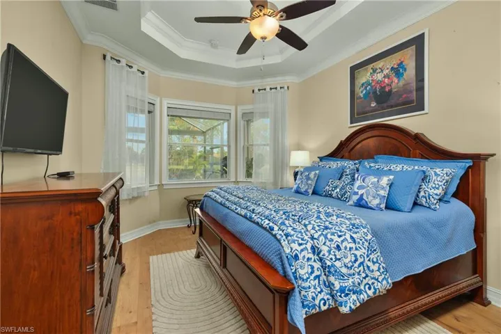 Bedroom featuring ceiling fan, ornamental molding, a tray ceiling, and light hardwood / wood-style flooring