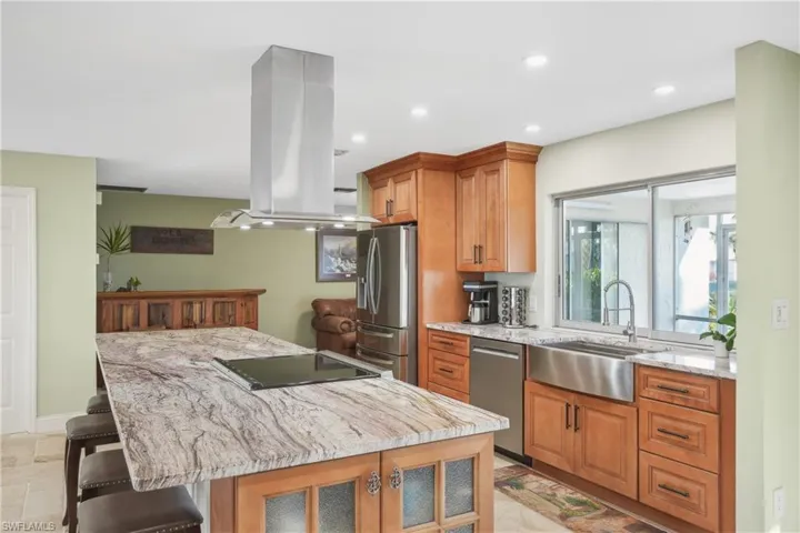 Kitchen featuring a kitchen bar, appliances with stainless steel finishes, island range hood, and light stone countertops