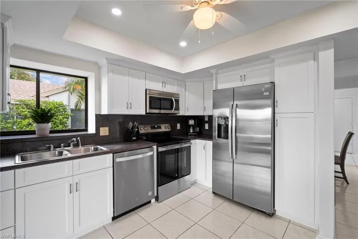Kitchen with tasteful backsplash, stainless steel appliances, white cabinets, sink, and ceiling fan